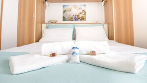 A neatly made bed with white linens, a blue pillow, and a small decorative item on the headboard. - Apartments Alba - Studio apartment (Rovinj)