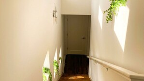 Un escalier étroit avec des marches en bois, des murs blancs et une petite fenêtre en haut.