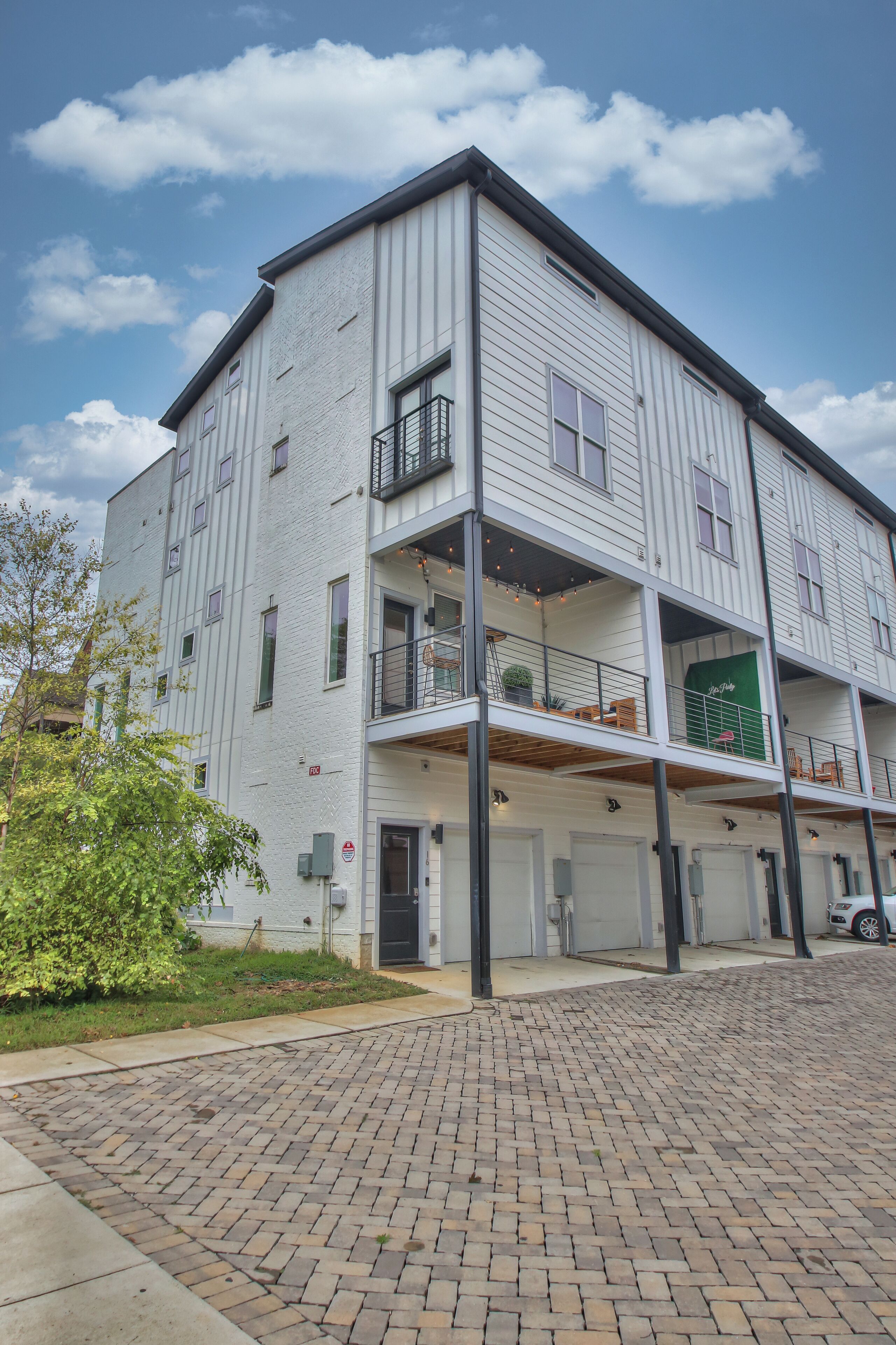 A multi-story building with a brick-paved ground floor, a balcony on the second floor, and a green awning on the third floor.