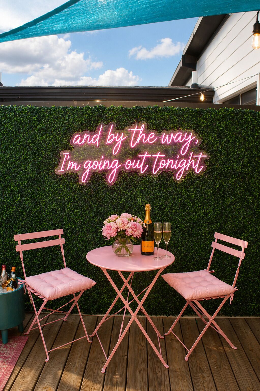 Une terrasse agrémentée d’une enseigne au néon, de deux chaises roses, d’une table et d’une bouteille de champagne.