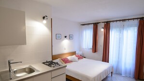 Hotelkamer met een bed, een klein kitchenette, een raam met gordijnen en een wandlamp.