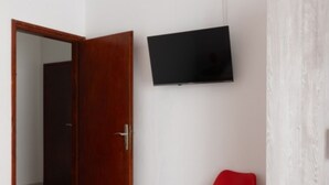 Una habitación con puerta de madera, televisor de pantalla plana en la pared y una silla roja.