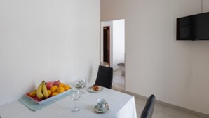 Un comedor con una mesa dispuesta para dos, un frutero y un televisor montado en la pared.