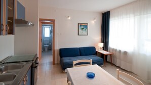 A compact living space with a kitchenette, a dining area, a sofa, and a view of the outdoors. - Apartments Alba - Three Bedroom Apartment (Rovinj)