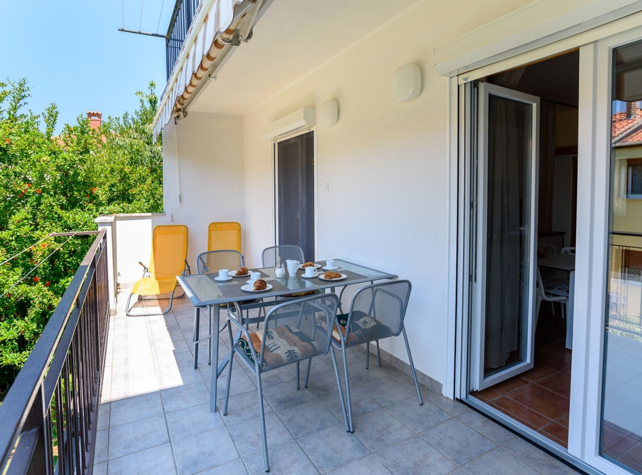 A balcony with a table set for two, chairs, and a sliding glass door leading to an interior space.