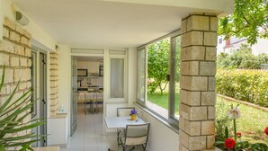 A balcony with a table and chairs, a view of the garden, and a stone wall. - Apartments Alba - Two Bedroom apartment (Rovinj)
