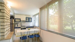 Een compacte keuken met een eethoek, met een stenen muur, een inbouwoven en een groot raam met zonwering.