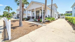 A two-story house with a covered porch, palm trees, and a well-maintained lawn.