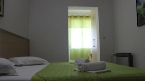 Ein Hotelzimmer mit zwei Betten, einer grünen gesteppten Bettdecke, einem zusammengerollten Handtuch und einem Fenster mit grünen Vorhängen.