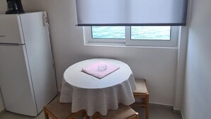 Una habitación pequeña y ordenada con una mesa redonda, dos sillas, un refrigerador y una ventana con persiana enrollable.