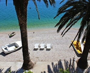 A beach with a row of white lounge chairs, a small boat, and a yellow boat on the shore.