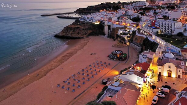 An aerial view of a coastal town with a beach, rows of beach umbrellas, and buildings with balconies overlooking the sea. - Albufeira - Anna Town (Albufeira)