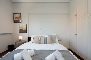 A neatly arranged hotel room with a bed, bedside table, lamp, and wardrobe. - Luxe Bliss – 2BR, Glyfada (Glifada)