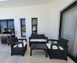 A balcony with wicker furniture, a grill, and a view of the city. - Villa Tranquila: Luxury Villa in Sosua Ocean Village, Dominican Republic (Sosua)