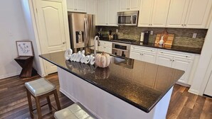 A modern kitchen with white cabinets, a central island with stools, stainless steel appliances, and a backsplash with a mosaic tile pattern. - 3Bedroom House in a family orientated neighborhood (Chula Vista)