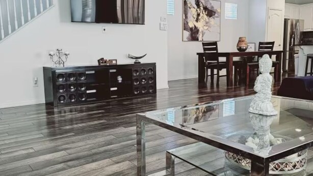 A spacious living room with a glass coffee table, dark wooden flooring, a black entertainment unit, and a dining area with a chandelier. - 3Bedroom House in a family orientated neighborhood (Chula Vista)