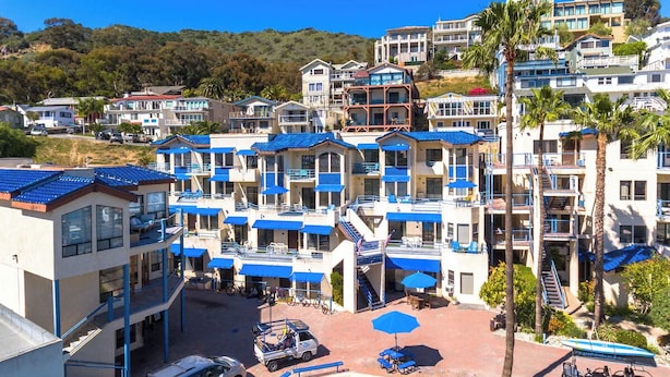 A multi-story hotel with balconies, a parking area, and a view of a hillside.