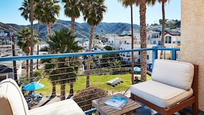 A balcony with a white sofa, a wooden table, and a magazine. There are palm trees and a view of a town and mountains in the background.