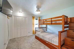Un dormitorio con una cama litera, ventilador de techo, televisor montado en la pared y un armario con puertas persianas.