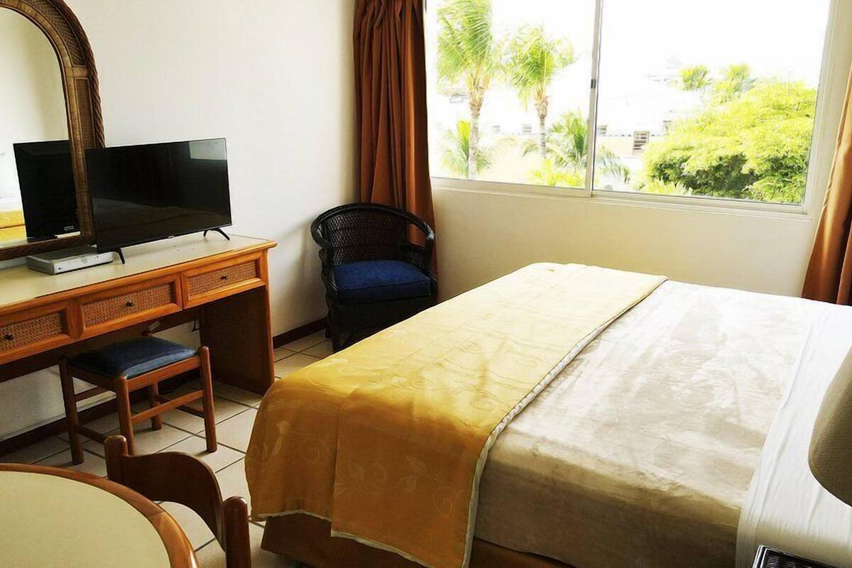 A hotel room with a bed, a desk with a television, a chair, and a window with curtains.