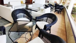 A modern lounge area with wicker chairs and a glass-top table, white sofas, and a view of the outdoors.