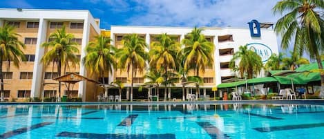 A hotel with a swimming pool, palm trees, and a clear blue sky.