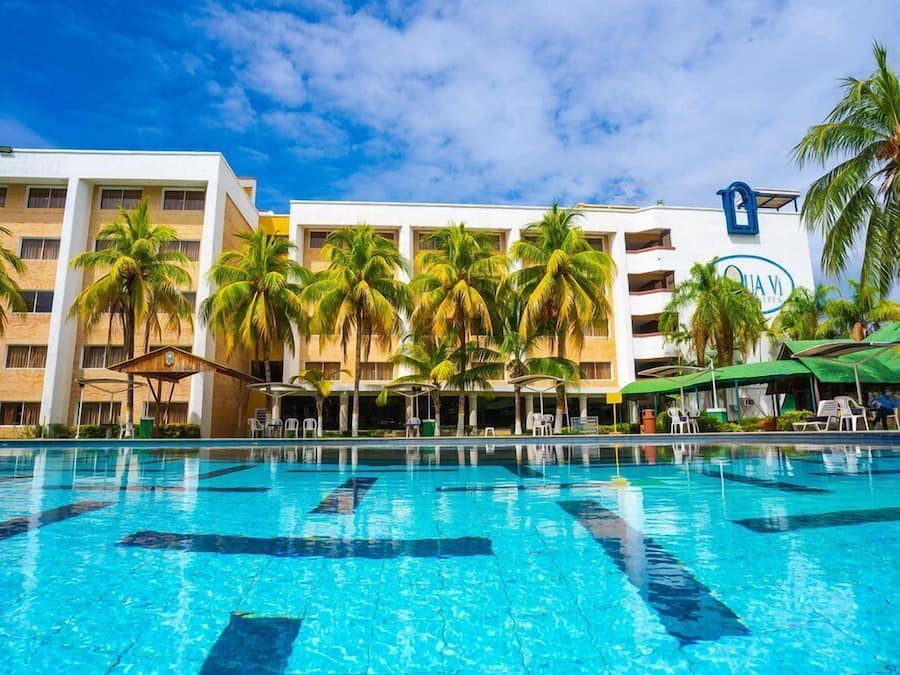 A hotel with a swimming pool, palm trees, and a clear blue sky.