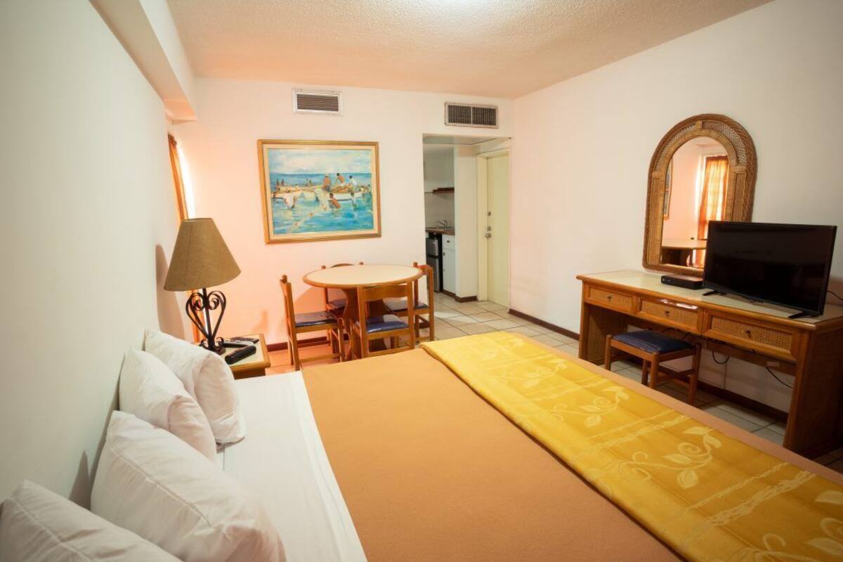 A hotel room with a bed, a desk, a television, a painting, and a mirror.
