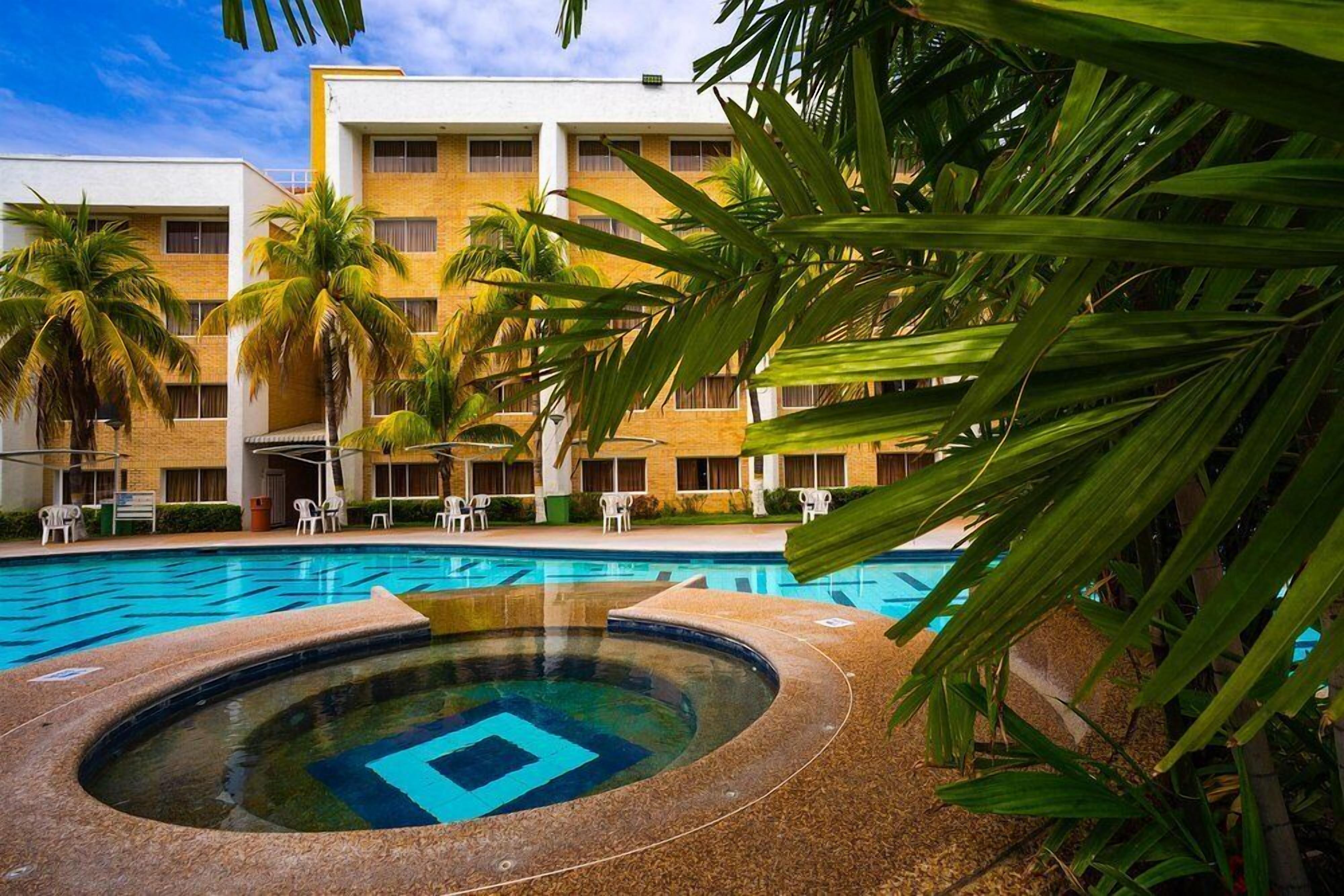 Un hotel con piscina, palmeras y un edificio con varios balcones.