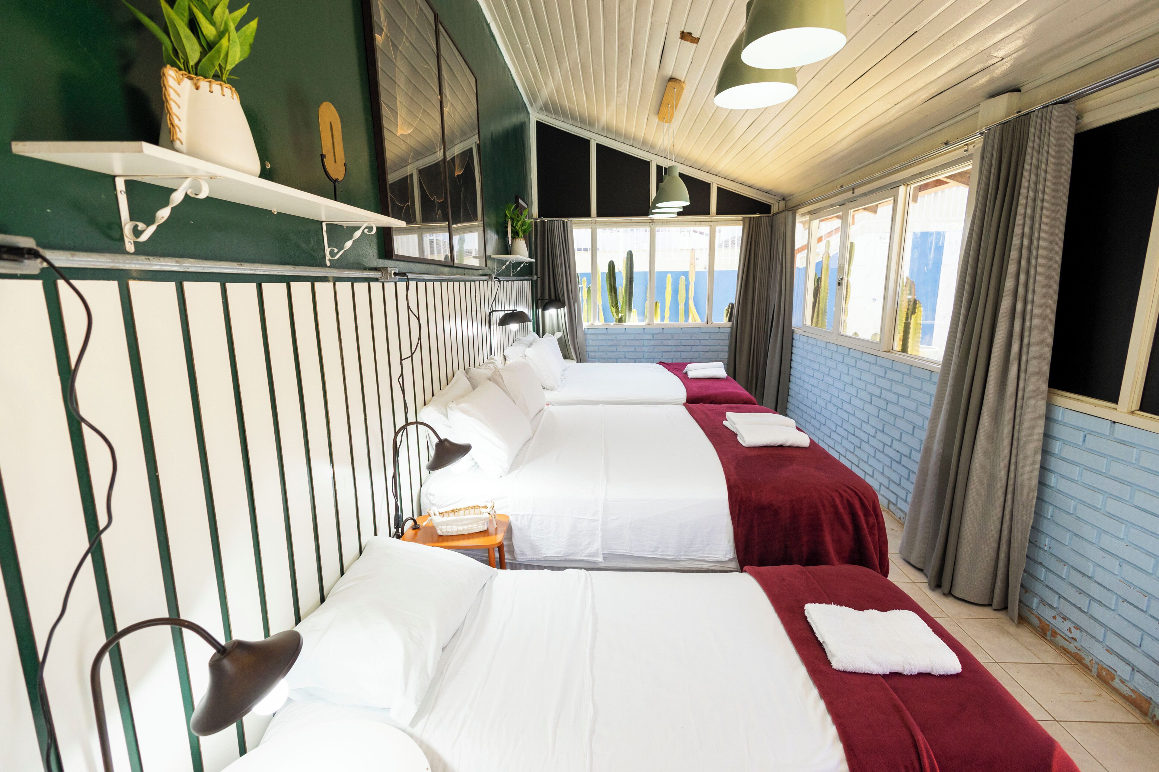 Una habitación de hotel con una cama grande, una mesita, una lámpara, una planta en maceta y una ventana con cortinas.