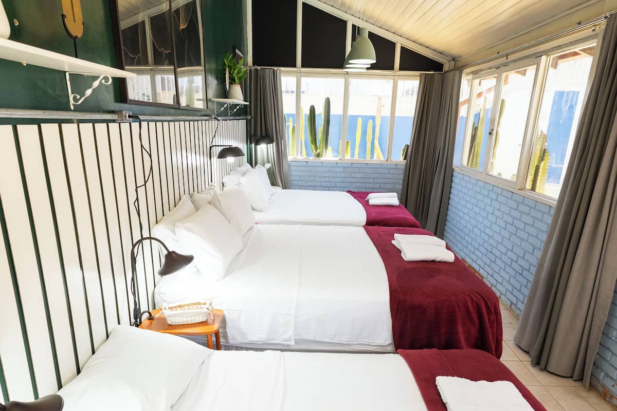 A hotel room with three beds, a round table, and a large window with curtains.
