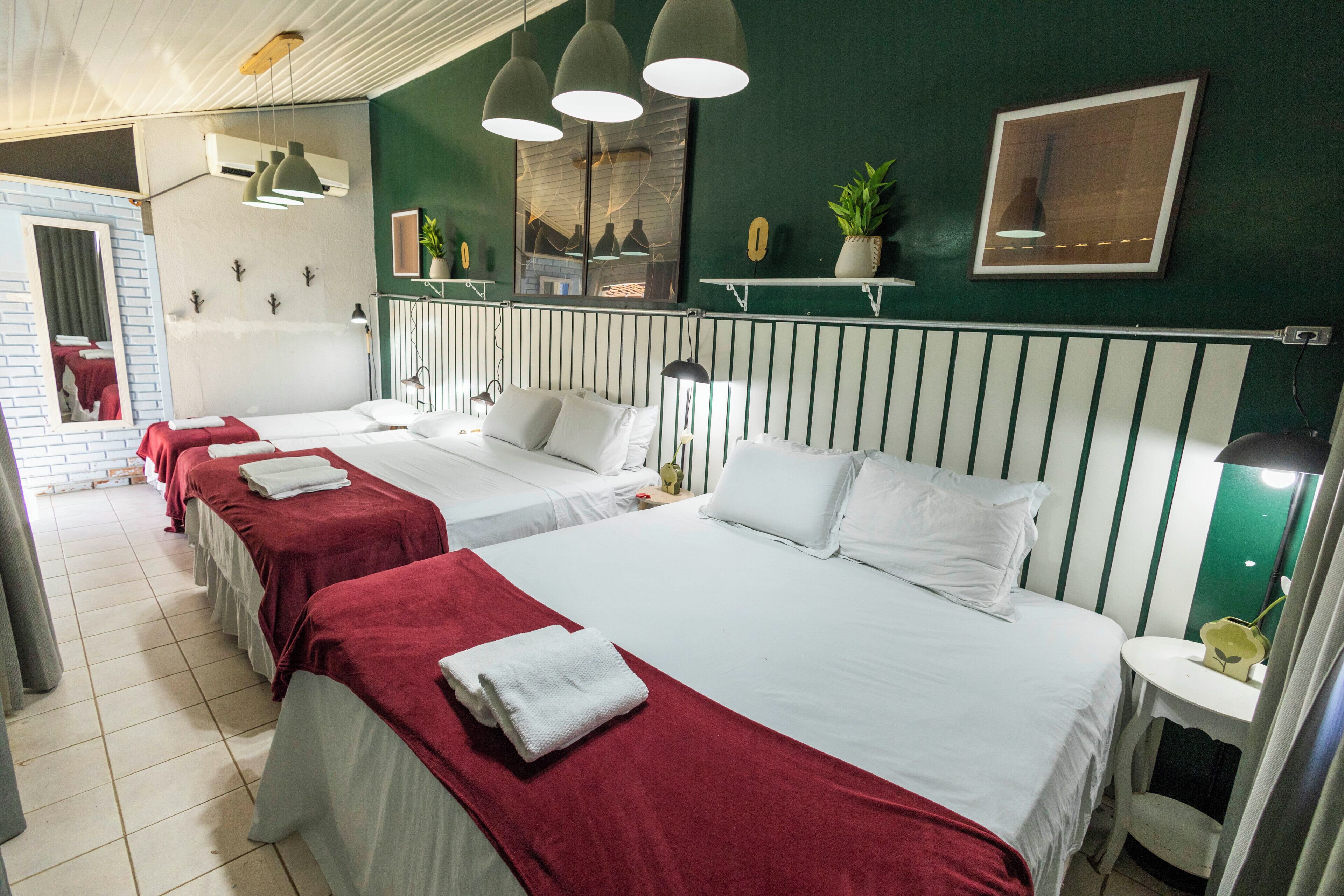 A hotel room with three beds, a mirror, a plant, and a small table.