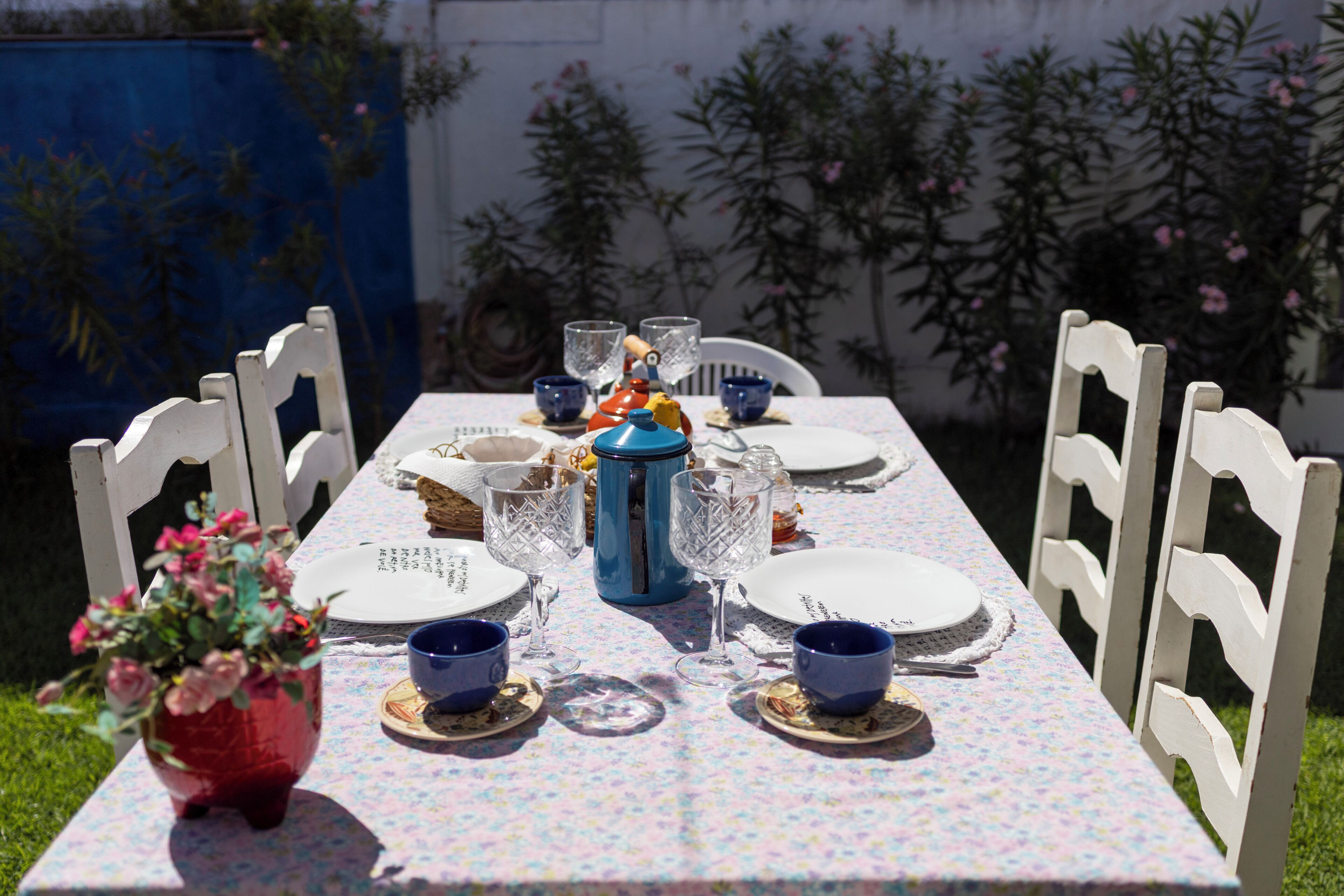 A table set for a meal with white chairs, a vase of flowers, and blue tableware.