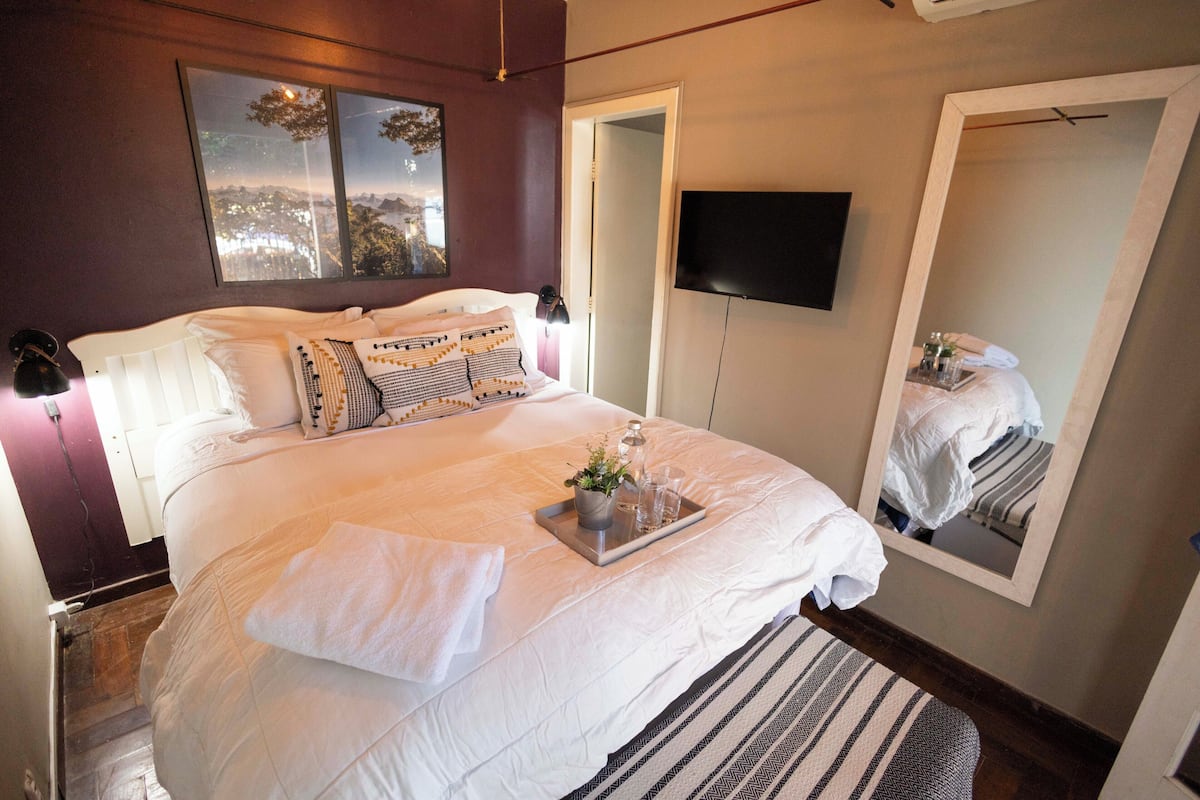 A neatly made bed with pillows, a tray with a plant, and a mirror.
