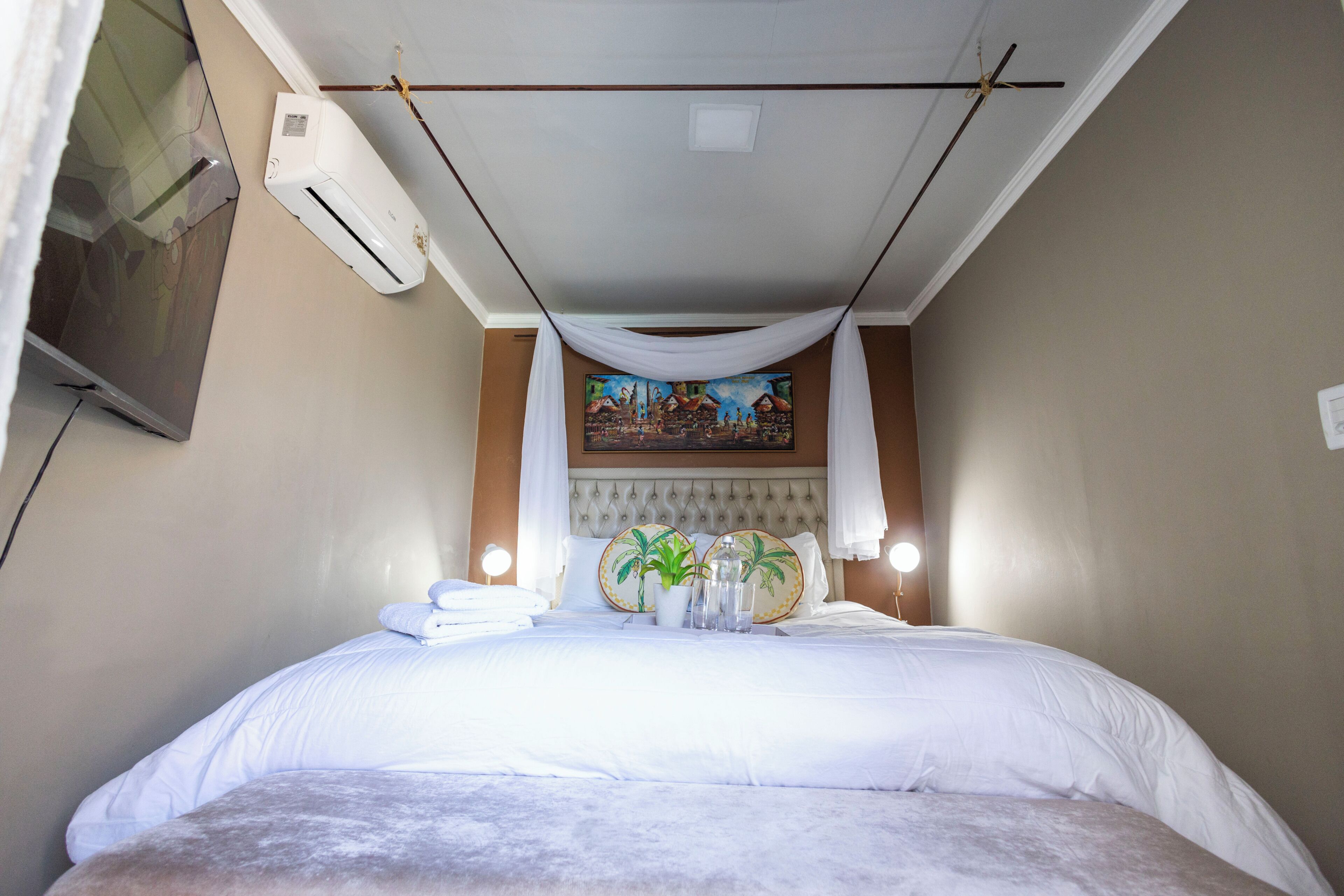 Una habitación de hotel con cama, aire acondicionado de pared, un cuadro y ventilador de techo.