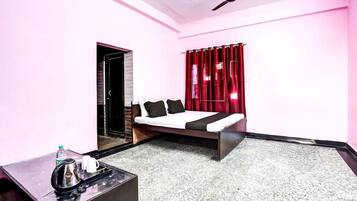 A bedroom with a bed, a bedside table, a water bottle, a kettle, and a ceiling fan.