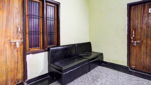 A room with a black leather sofa, wooden doors with metal bars, and a tiled floor. - Hotel Radhey inn (Kanpur)