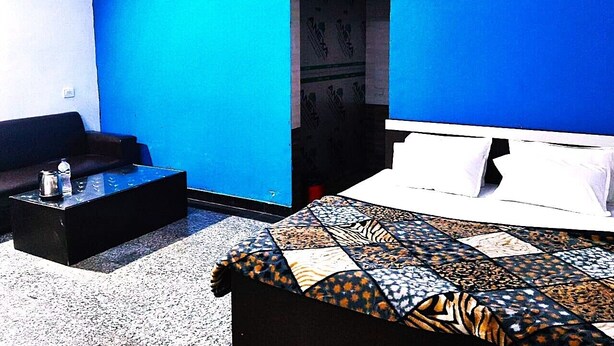 A room with a bed, a sofa, a small table, and a door leading to another room. - Hotel Radhey inn (Kanpur)