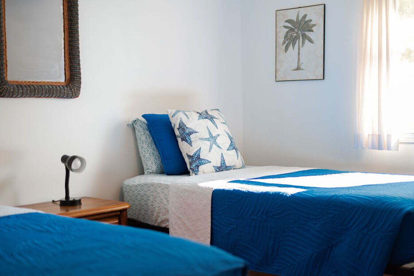 A bedroom with two beds, a nightstand, a lamp, a wall-mounted mirror, and a framed picture.
