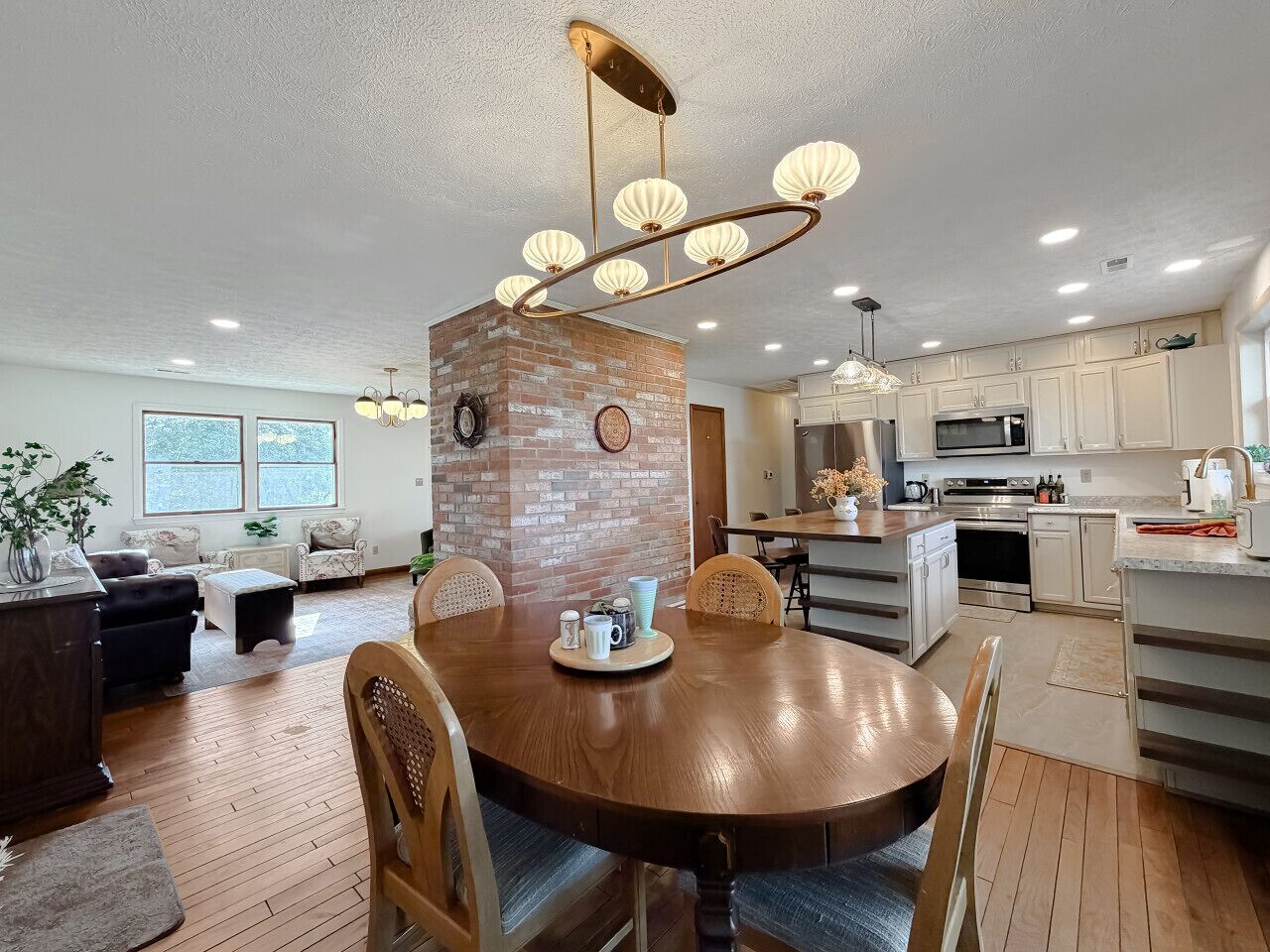 A modern kitchen with white cabinets, a brick accent wall, and a dining area with a round wooden table and chairs.