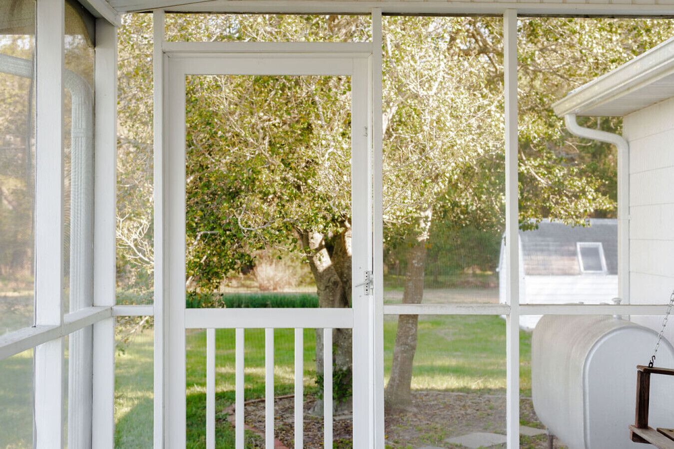 A covered porch with a view of a tree and a house in the background.