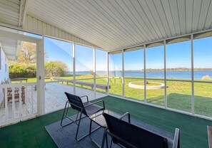 A covered patio with a view of a lake, furnished with chairs and a table.