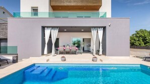 A modern house with a swimming pool, a patio with outdoor furniture, and a view of the interior. - Villa Fažana (Fažana)