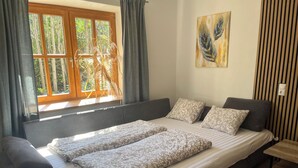 Una cama doble con cubrecama estampado, una ventana con cortinas, un cuadro colgado en la pared y un panel rayado en la pared.