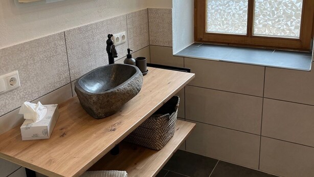 Un baño moderno con un lavamanos de piedra, estantes de madera, una ventana con vistas y un espejo.