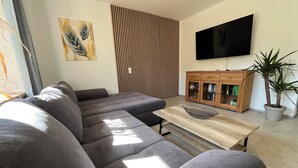 Una sala de estar moderna con un sofá seccional, un mueble de madera, un televisor de pantalla plana y una planta en maceta.