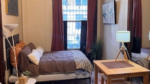 A bedroom with a bed, a desk, a chair, a lamp, a large mirror, and a window with curtains. - One bedroom  in United States of America, New York (New York)