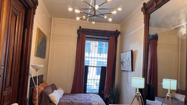 A bedroom with a bed, a desk, a chair, a lamp, a mirror, and a window with curtains. - One bedroom  in United States of America, New York (New York)