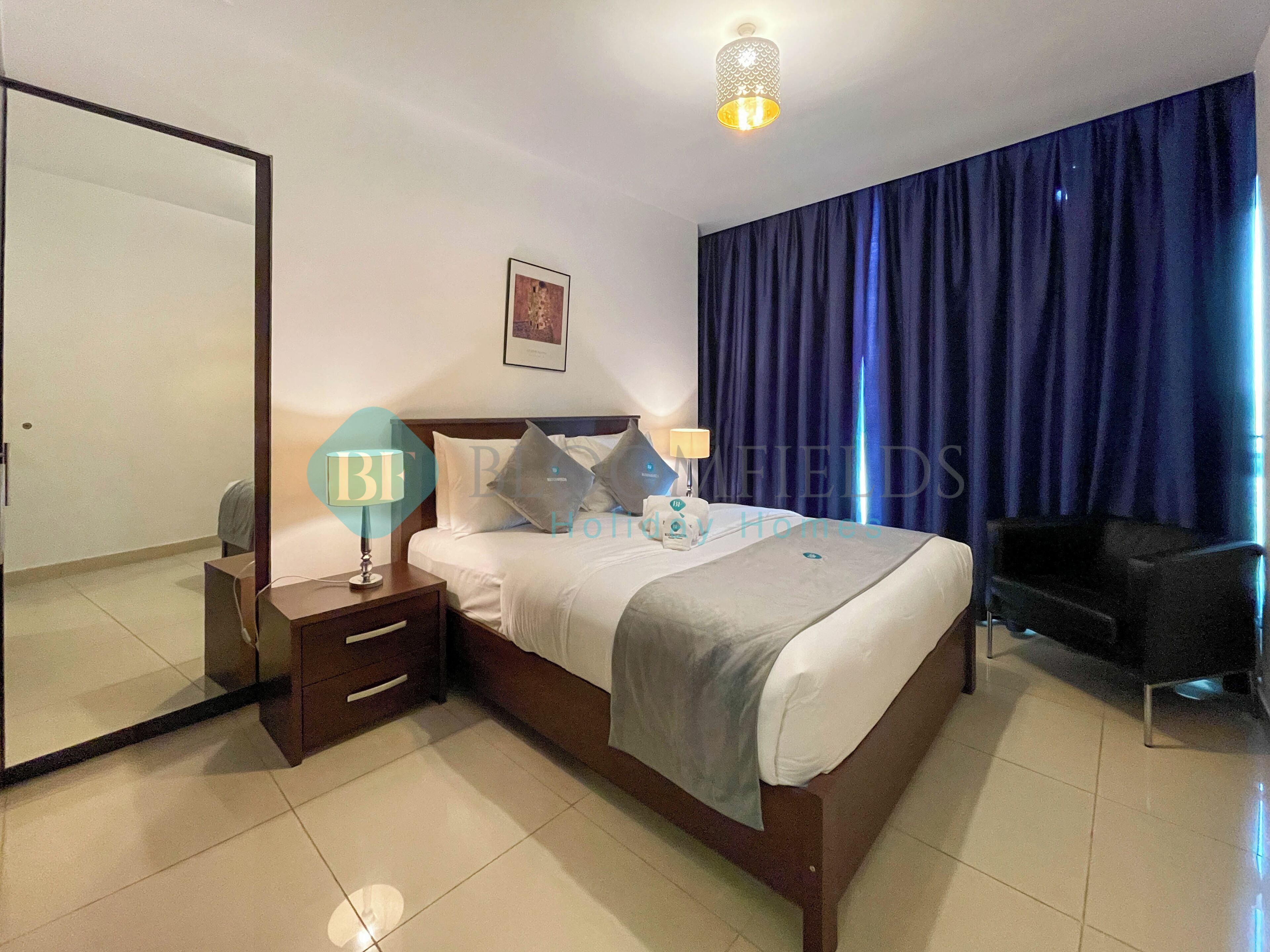 A hotel room with a bed, bedside table, lamp, and a large mirror.