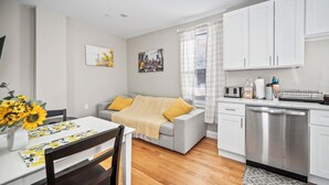 A modern kitchen with white cabinets, a built-in dishwasher, and a dining area with a table and chairs.